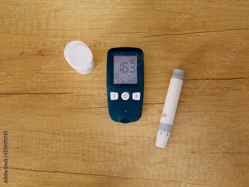 A glucometer rests on a wooden table showing a blood sugar level of 163 mg dL. This indicates a very high sugar level related to diabetes management.