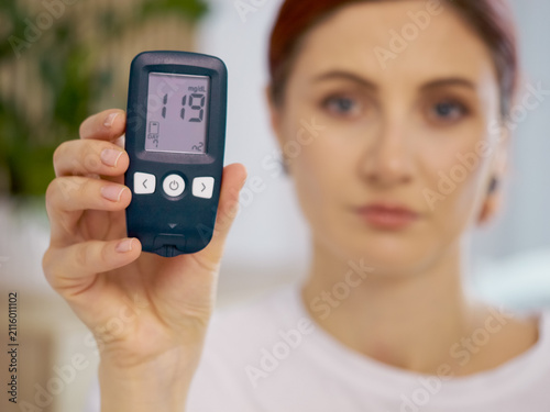 A woman holds a glucometer showing a reading of 119 mg dL while discussing blood sugar levels. This moment emphasizes the importance of monitoring glucose health.