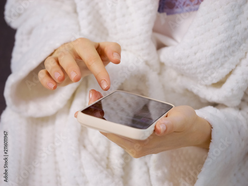 A woman holds a smartphone while swiping and engaging with friends at home. The setting is warm and inviting, focusing on her hands and phone activity.