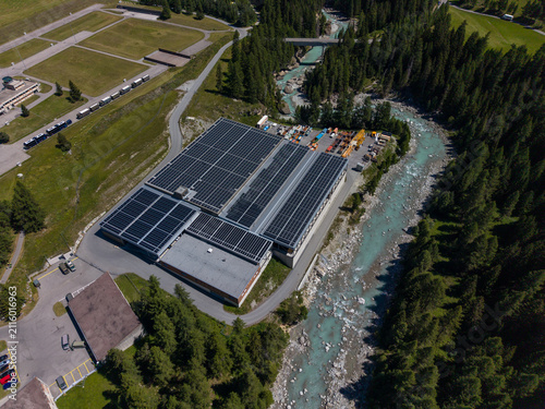 Aerial view of the Upper Engadine Wastewater Treatment Plant featuring extensive rooftop solar panels, situated beside the turquoise waters of the Inn River in S-chanf, Grisons, Switzerland.