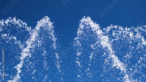 Close up of sparkling fountain water splashes against a blue sky. Refreshing droplets create a dynamic abstract background that represents freshness, summer, energy, and motion