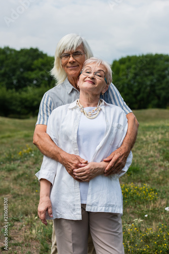 Obraz na płótnie Loving seniors embrace on a sunny hill, celebrating their lifelong romance