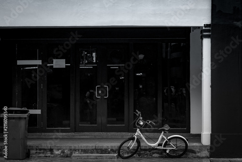 Фотография Minimal black and white street scene with bicycle parked outside modern storefront, quiet urban lifestyle concept representing simplicity, sustainability, solitude and contemporary city living