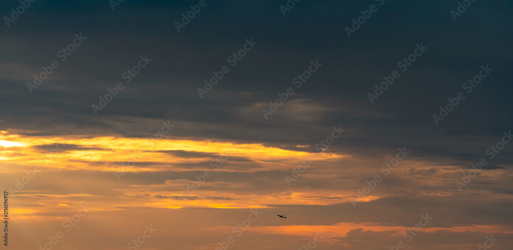 Fototapeta premium Commercial airplane flying beneath dramatic sunset clouds with expansive copy space, symbolizing air travel, aviation, tourism, freedom, business transportation and memorable journey at golden hour.