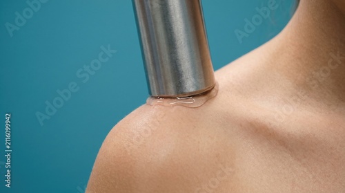 Close up of physical therapy ultrasound device applying conductive gel on female shoulder and collarbone