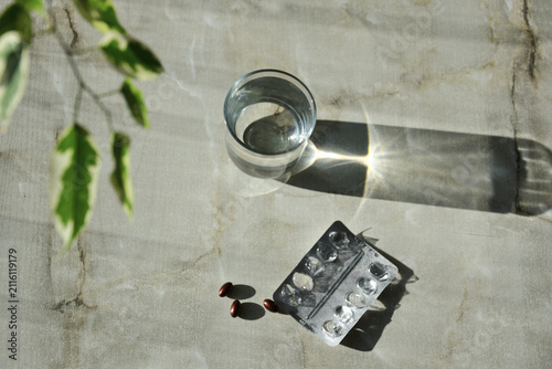 Glass of water and medication pills with plant shadows on stone surface