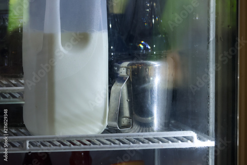 Milk jug metal pitcher on refrigerator shelf chilled kitchen scene with soft reflection and subtle mood