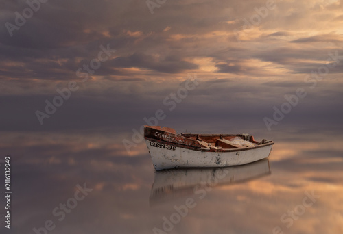 Composite of a fishing boat with reflection in shallow water and a cloudy sky