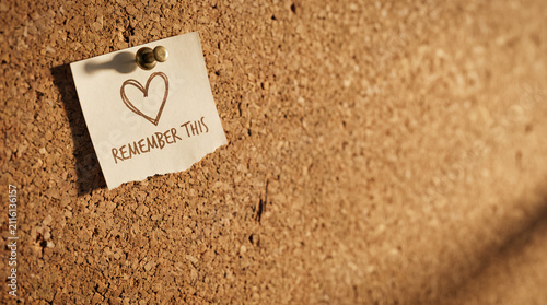 Cork bulletin board background with pinned sticky note paper featuring handwritten remember this and heart