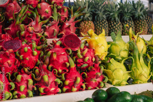 Vibrant tropical market scene featuring red and yellow dragon fruits, pineapples, and fresh exotic produce arranged for sale.