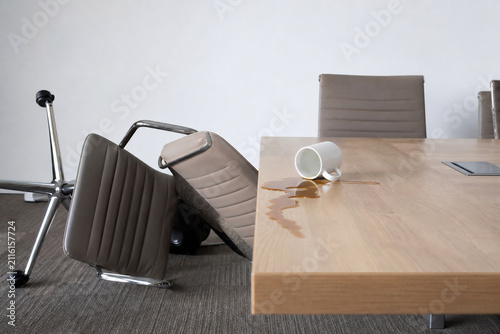 Overturned chair and spilled coffee by conference table, office insult aftermath concept