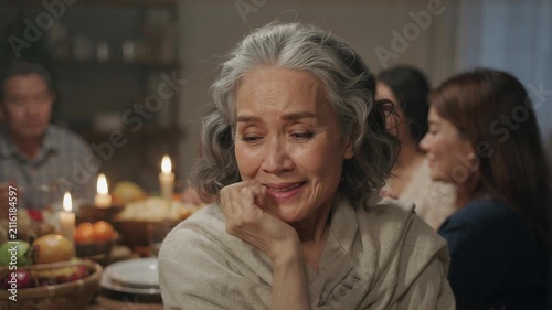 Emotional senior Asian woman smiling through tears at dinner table