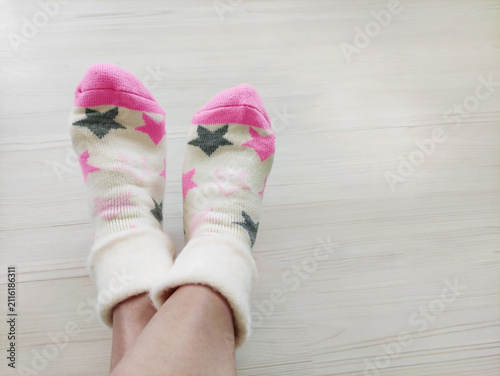 Feet wearing soft knitted patterned socks on a light wooden floor. Cozy domestic shot from a side view, concept of comfort, warmth, relaxation, leisure, and casual home fashion