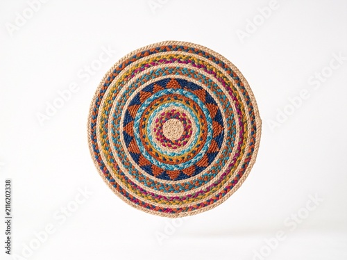 Handwoven circular jute mat or coaster featuring colorful geometric patterns and intricate braided textures isolated on a white background for home interior decoration and rustic dining table