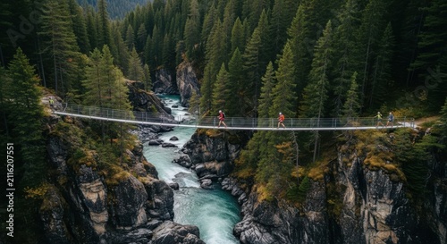 Two hikers traverse a suspension bridge over a rushing river through a lush green forest canyon