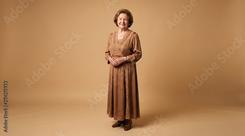 Full length portrait of a smiling elderly woman wearing an elegant brown dress against a warm backdrop