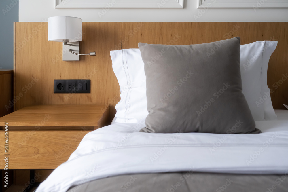 Obraz premium Bedroom interior showcasing a clean bed with white linens, a comfortable gray pillow, reading lamp, and a wooden headboard with an integrated bedside table and electrical outlets