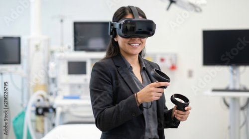 A young Hispanic woman with long black hair wears a VR headset and holds controllers in a modern medical training room with equipment in the background.
