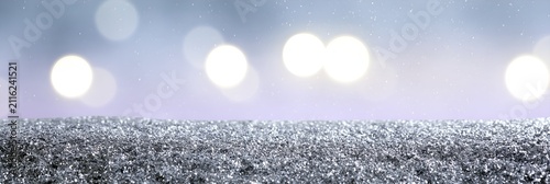 Glistening snowflakes scatter across dark, textured ground. Soft bokeh lights glow in the blurred background