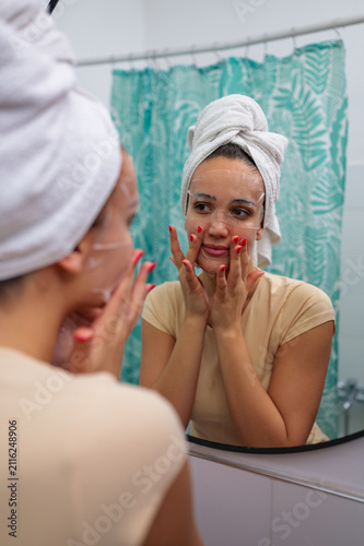 Canvas Print Young woman with a towel wrapped around her hair applying a hydrating sheet mask
