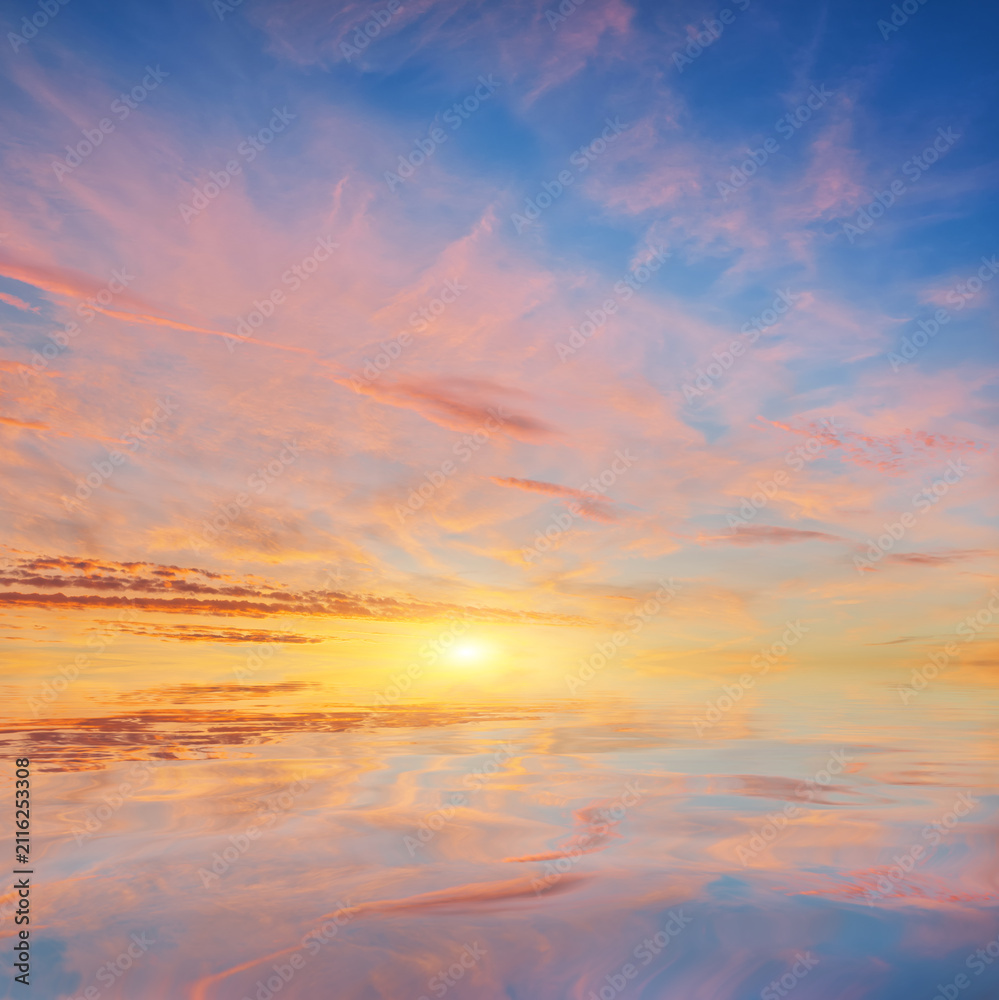 Fototapeta premium Beautiful golden sunset sky with pink clouds reflecting in the calm water surface.