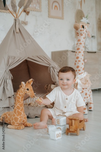 a child plays in a children's room with a teepee, wooden blocks, and a car on the floor among stuffed giraffes, a small boy playing at home