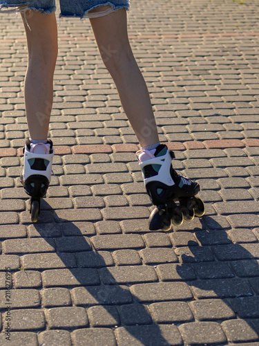 Close up of teenage girl's feet wearing inline roller skates on a paved walkway during a summer outdoor activity. Concept of active lifestyle, movement, fitness and urban recreation.