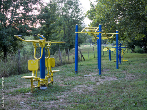 Gimnasio al aire libre en un parque entre la naturaleza donde se pueden observar las máquinas de hacer ejercicio entre los árboles.