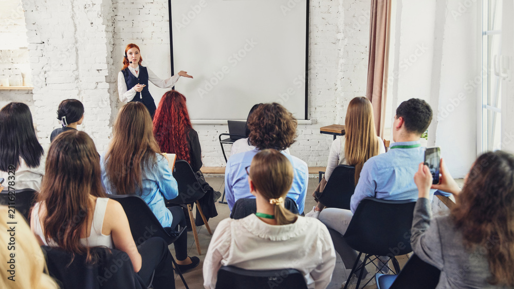 Obraz premium Presenter explaining topic to attentive audience in business seminar room. Concept of corporate training, professional education, workshop, coaching, and conference content.