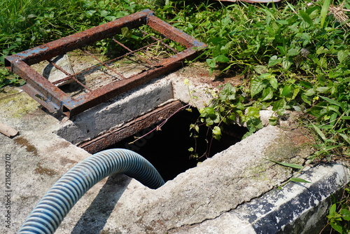 Rusty metal grate and hose near an open well or septic tank opening.