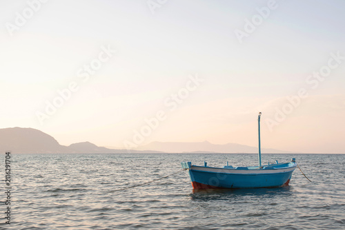Canvas Print Small greek boat in the sea at sunset with mountains on the background