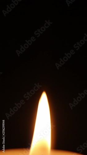 A match lights a candle. The candle flame begins with a small flicker near the wick and gradually grows against a dark background, turning into a tall vertical flame that burns calmly and steadily.