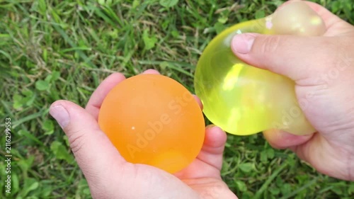 ASMR close-up of hands squeezing and stretching orange and yellow slime balls on green grass, repeatedly forming soft textures in a slow, satisfying, relaxing motion.