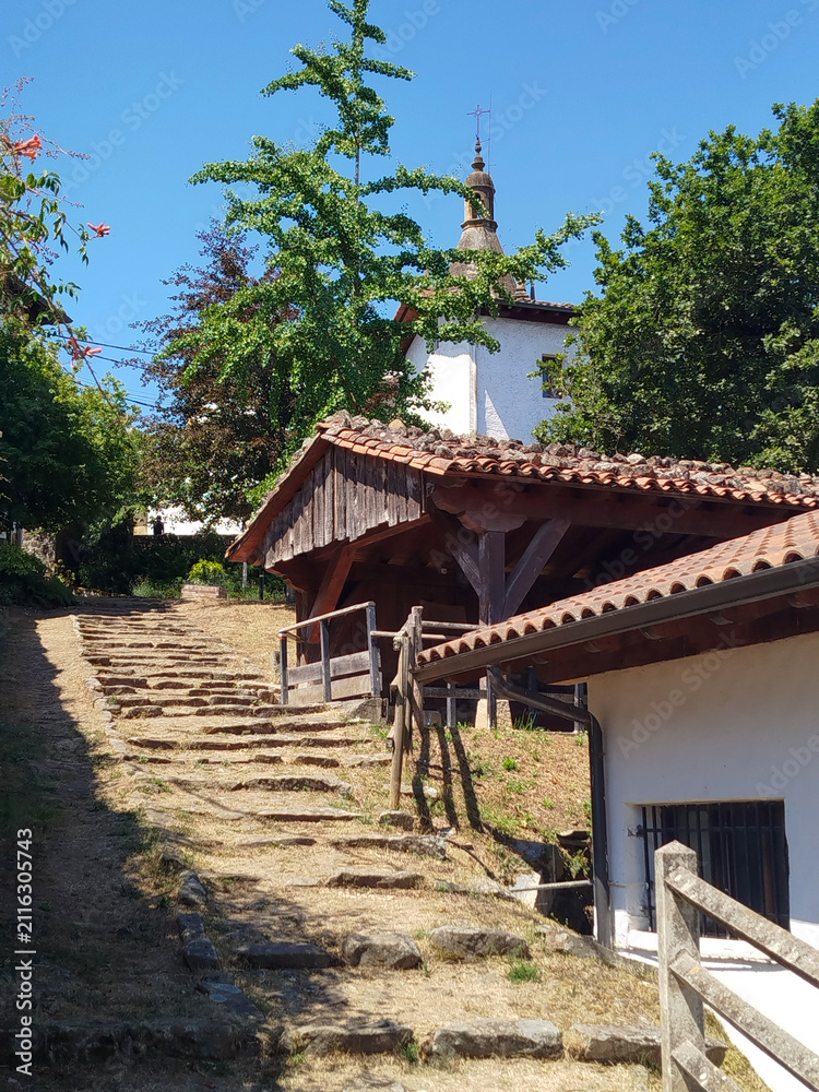 Fototapeta premium Escalinata rústica de piedra hacia casas tradicionales bajo árboles verdes en Zerain, Guipuzcoa, España