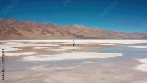 Lone traveler standing on expansive salt flat landscape under clear blue sky, surreal desert vista photography.