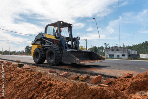 Fotografie Skid steer loader operated by worker on asphalt road during paving and roadwork