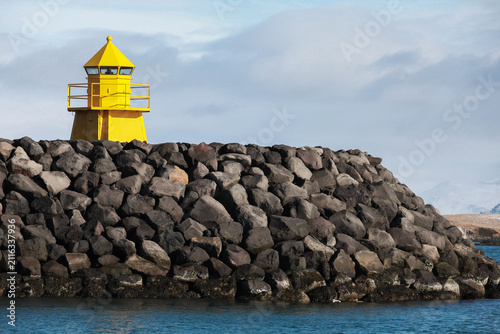 Yellow lighthouse tower stands on a stone breakwater at the entrance to the main port of Reykjavik city, Iceland