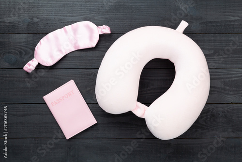 Pink travel pillow with sleeping mask and passport on wooden background, top view