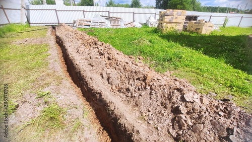 Foto Suburban Earthworks Long narrow excavated ditch in green lawn next to white fenc