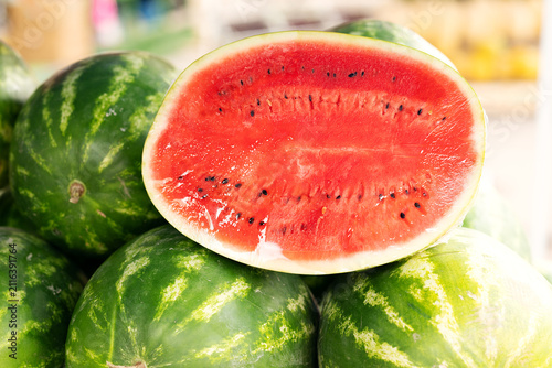 Halved ripe watermelon wrapped in plastic foil sitting on top of whole melons at market stall.