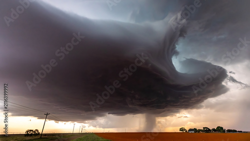 View of a massive supercell storm cloud with a rotating funnel over a rural field with power lines in Oklahoma City, Oklahoma, United States.
