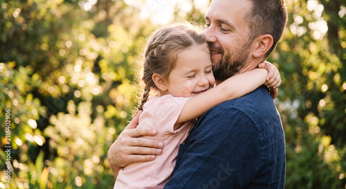 Happy young father hugging his little daughter outdoors in summer park.