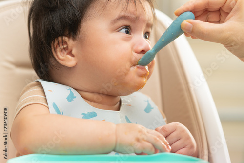 Baby being fed with a silicone spoon in a high chair during complementary feeding. Infant nutrition, parenting and childcare concept.