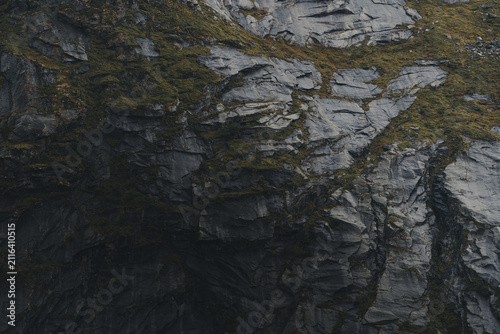 View of the rugged, dark, rocky cliff face of Lofoten with patches of green moss and textured stone surfaces, Nordland, Norway.