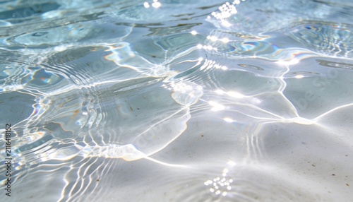 Glittering clear shallow water surface casting sunlit caustic light bands over pale bottom, specks