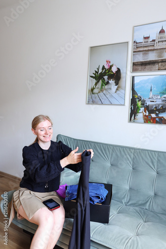 Female online seller presenting clothes before packing or listing them for sale, second hand fashion, online marketplace and home business.