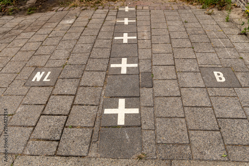 View of the international border line marked with white crosses on stone pavement separating the Netherlands and Belgium in Baarle-Nassau, North Brabant, Netherlands.