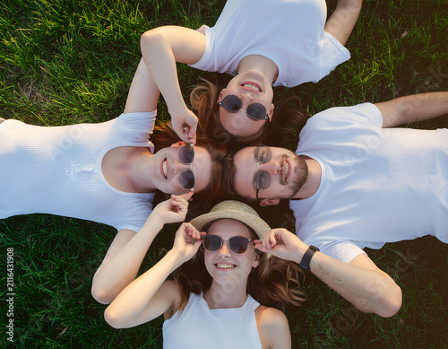 Overhead View of Happy Young Friends Lying on Green Grass Circle Facing Camera