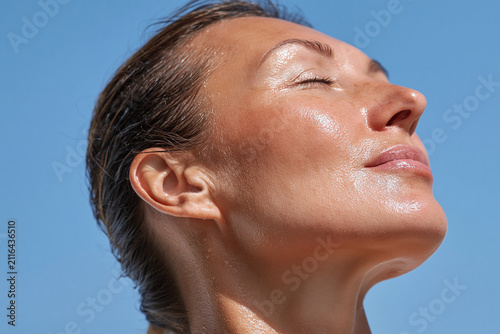 Glowing luminous skin close up, radiant hydrated cheek and jawline, sunlit profile with closed eyes, serene skincare moment