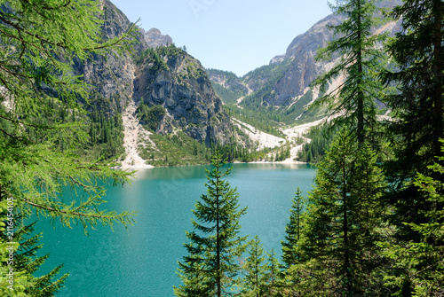 Panoramic view of Lake Braies (Pragser Wildsee) framed by evergreen trees, turquoise alpine water and dramatic Dolomite peaks on a clear summer day in South Tyrol, Italy.